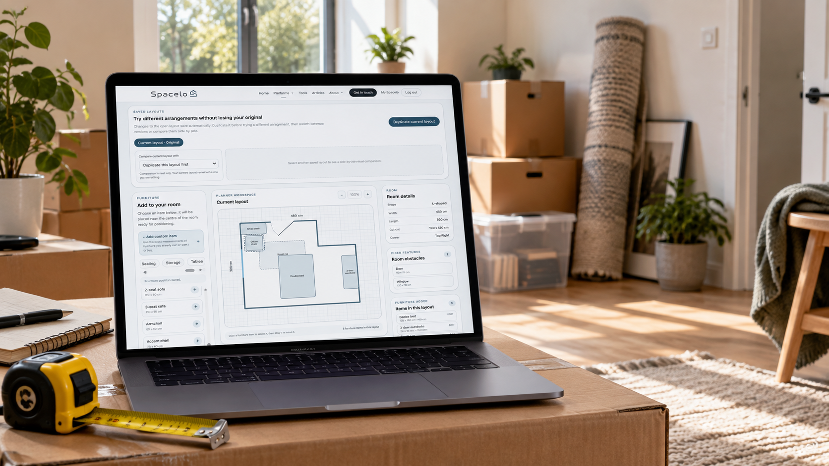 Laptop displaying the Spacelo Room Layout Planner in a partially cleared room with moving boxes and a tape measure.